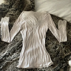Ljusgrå intimissimi topp med spets - Supersnygg ljusgrå långärmad topp från Intimissimi med v-ringning och detaljerad spets runt halsringningen och ärmsluten. Tunn och mjuk i bomullsmix, perfekt för dig som gillar romantiska vibes och vill ha något extra till din outfit.