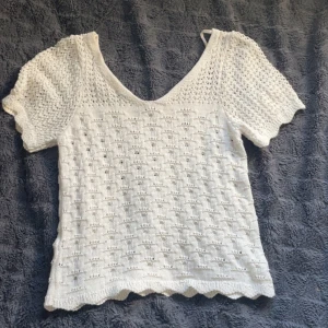 Vit stickad blus med v-ringning - Superfin vit stickad blus med v-ringning. Blusen har ett hålmönster över hela plagget och vågig kant nertill.