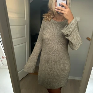 Beige stickad klänning från Noisy May - Supermysig beige stickad klänning från Noisy May med lång ärm och rund hals. Modellen är kort och har en relaxed fit med lite utsvängda ärmar. Perfekt att styla med boots eller sneakers för en chill look.