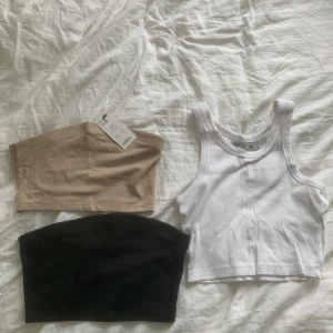 3-pack toppar: vit ribbad crop, beige & svart tubtopp - Säljer ett set med tre toppar: en vit ribbad croppad linnetopp med breda axelband, en beige tubtopp och en svart tubtopp. Alla är i mjuk bomull och perfekta för sommaren. Stilrena och enkla att matcha till olika outfits.