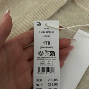 Beige omlottkofta från Gina Tricot - Superfin ljusbeige omlottkofta från Gina Tricot med knytband i sidan och breda ribbade muddar. Mjuk och stickad med v-ringning, perfekt för lager på lager. Enkel att styla och riktigt cozy till höst och vinter.