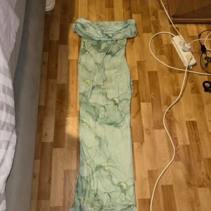 Ljusgrön offshoulder långklänning - Säljer en ljusgrön långklänning med offshoulder-modell och marmorerat mönster i gröna och gula toner. Klänningen har en figurnära passform och är tillverkad i ett tunt, stretchigt material. Perfekt för dig som vill sticka ut med en unik look.