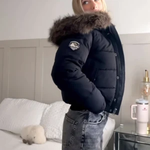Superdry Everest Puffer Jacka - Säljer en svart pufferjacka från Moose Knuckles med stor huva och fuskpäls. Jackan har ribbade muddar, dragkedja och knappar framtill samt två stora fickor. Perfekt för kalla dagar och riktigt snygg till jeans.