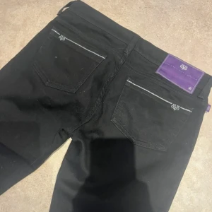 Victoria Beckham jeans! - Svarta jeans från Victoria Beckham  med lite bolotcut och raka ben och låg midja. Snygga detaljer med lila patch och broderad logga på bakfickorna. Tillverkade i stretchig denim av 99% bomull och 1% spandex för skön passform.