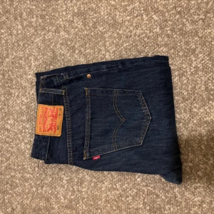 Levi's 501 mörkblå jeans - Klassiska Levi's 501 jeans i mörkblå denim. Rak passform med fem fickor, snygga kontrastsömmar och ikonisk läderpatch bak. Perfekta för dig som gillar tidlös stil och vill ha ett par jeans som funkar till allt. Strl W32 L32.