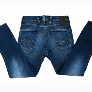 Replay Anbass Hyperflex jeans - Snygga Replay Anbass Hyperflex jeans i klassisk blå tvätt med slitningar och coola detaljer. Storlek: W31 o L30. Byxorna har raka ben och fem fickor. Säljer på grund av att de är för små. Pris går att diskutera..
