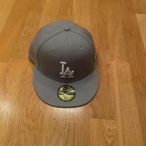 Grå LA-keps från New Era 59FIFTY, aldrig andvänt helt ny! - Snygg grå 59FIFTY keps från New Era med LA-logga framtill i vitt. Klassisk flat peak och broderad MLB-logga bak. Tillverkad i polyester och passar dig som gillar streetwear och sportig stil. Helt ny aldrig andvönd!
