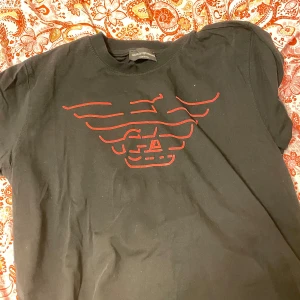 Svart t-shirt från Giorgio Armani - Svart t-shirt från Giorgio Armani med rött tryck av den klassiska örnloggan på bröstet.  