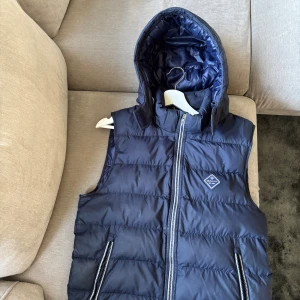 Mörkblå väst från GANT - Säljer min Gant Väst då jag ej använder den längre. Storlek small/17. Den passar för M, Huvan går å ta av 