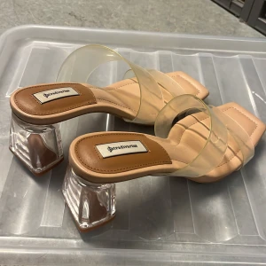Stradivarius sandaler med transparent klack - Snygga sandaler från Stradivarius i beige med transparenta remmar och fyrkantig tå. Klacken är i genomskinlig plast och har en unik, kantig form. Perfekta för dig som vill sticka ut med en modern och trendig look.