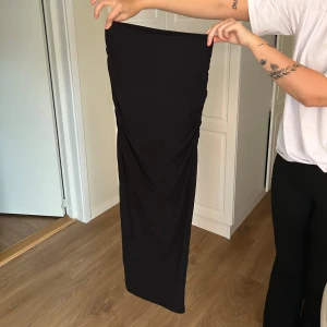 Svart långkjol från Gina Tricot - Säljer en svart långkjol från Gina Tricot i storlek S. Kjolen är figurnära med snygg rynkdetalj längs benen och har en enkel, stilren design. Perfekt för dig som gillar minimalistiska plagg med en twist. Säljer pga använder ej 