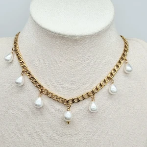 Guldhalsband med droppformade pärlor - Snyggt halsband i guldtonad kedja med sju droppformade vita pärlor som hänger längs länkarna. Kedjan har en klassisk design och pärlorna ger en elegant och trendig vibe. Perfekt för att lyfta din outfit med lite extra bling.