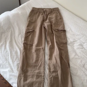 Beiga cargobyxor med fickor - Snygga beiga cargobyxor med stora sidofickor och raka ben. Byxorna har normal passform och är tillverkade i bomull, vilket gör dem både bekväma och lätta att styla. Perfekta för en avslappnad och trendig look.