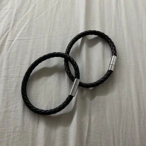 Två flätade armband i svart och brunt - Säljer två stilrena armband i flätad design, ett svart och ett mörkbrunt. Båda har magnetlås i silverfärgad metall och passar perfekt för en enkel men snygg look. Armbanden är gjorda i konstläder och känns både lätta och bekväma på handleden.