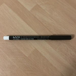 NYX vit ögonpenna SPE906 - Vit ögonpenna från NYX Professional Makeup i nyansen SPE906 White. Pennan har en klassisk träkropp med svart och vit design och är perfekt för att skapa ljusa detaljer eller öppna upp blicken. Enkel att vässa och smidig att använda för kreativa sminkningar. Vässad en gång.
