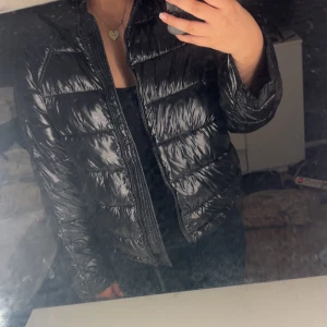 Svart glansig pufferjacka med huva - Säljer en svart, glansig pufferjacka från Zara med huva och dragkedja framtill. Jackan har quiltad design och är perfekt för kyligare dagar. Den har lång ärm och en riktigt snygg, modern look som passar till allt. Ny skick , pris går o diskutera 