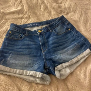 Blå jeansshorts från Lindex - Snygga blå jeansshorts från Lindex med klassisk femficksdesign och uppvikta benslut. Shortsen har normal passform och är tillverkade i slitstarkt denim med coola tvättade detaljer. Perfekta för en chill sommarlook. Sitter dock ganska långt ner. 