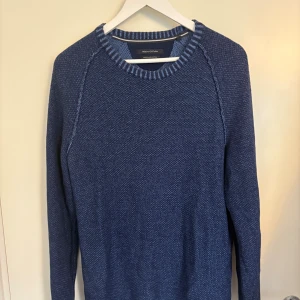 Blå stickad tröja Marc O'Polo M - Säljer en blå stickad tröja från Marc O'Polo i storlek M. Tröjan har en strukturerad bomullskvalitet, ribbade muddar och rund halsringning med snygga ränder. Perfekt för dig som gillar klassisk och stilren look.