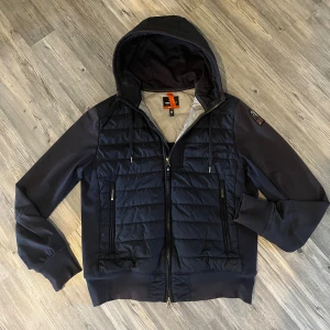 Mörkblå Parajumper cardigan - En riktigt fet cardigan med huva 🔥 från Parajumper som är mörkblå. Köpte för 2,959kr och säljes för 1500. Använd i ca 4 månader. Det är en storlek M men jag har S och den passar perfekt. Hör av er om ni är intresserad                                                     Original pris: 3700kr💨                                 (Kvitto finns)🧾