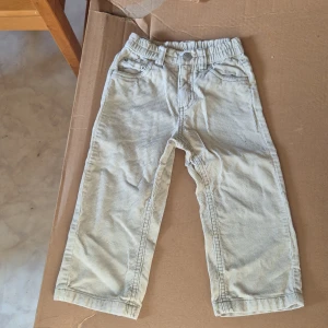 Beiga manchesterbyxor för barn - Snygga beiga manchesterbyxor från Boys Planet by Lindex i storlek 92. Byxorna har resår i midjan, klassiska fickor fram och bak samt ett broderat motiv på ena bakfickan. Perfekta för en cool och avslappnad stil.