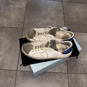 Philippe Model vita sneakers med blå detalj - Säljer ett par vita Philippe Model sneakers i mycket dåligt skick. Skorna behöver lagning på många ställen därav priset. Går inte att gå med skorna som de är nu, men för någon som vill chansa och lämna in till lagning. 