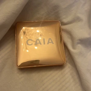 CAIA highlighter i guldig förpackning - Snygg highlighter från CAIA i en lyxig, guldig fyrkantig dosa med spegel. Pudret har en skimrande champagnefärg och en cool cirkelmönstrad yta. Perfekt för att ge glow till kindbenen eller andra highlights i ansiktet. I färgen Saint Tropez. Endast använd några gånger!💕