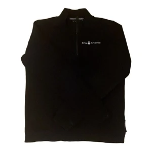 Svart Sail Racing half zip tröja - Svart långärmad tröja från Sail Racing med halv dragkedja och logga på bröstet. Tröjan har en stilren design och är perfekt för dig som gillar sportig och clean stil. Materialet är mjukt och passar bra till lager-på-lager.