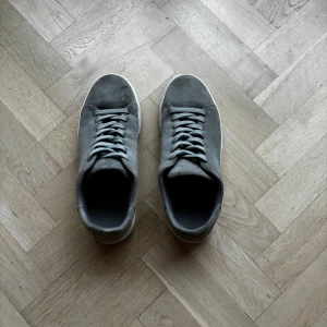 Grå mockasneakers med vit sula - Snygga grå Selected Homme i mocka med klassisk rund tå och platt vit sula. Skorna har grå snörning och en stilren, minimalistisk design som passar till det mesta. Perfekta för dig som gillar en clean och enkel look. Ordinarie pris är typ 1200 kr.Pris kan diskuteras!