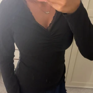 Svart långärmad topp från Anna Field - Svart långärmad topp från Anna Field med v-ringning och fina spetsdetaljer vid halsen. Toppen har rynk framtill som ger en snygg form och är tillverkad i mjukt material. Perfekt för dig som gillar stilrena och feminina plagg.