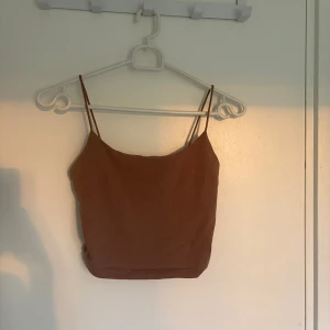 Brun croppad linnetopp från Shein - Säljer en brun croppad linnetopp från Shein i storlek XS. Toppen har tunna axelband och är tillverkad i mjuk bomull. Enkel och stilren design som är perfekt för varma dagar. Färgen är en varm brun ton och modellen är figurnära med en kortare passform.