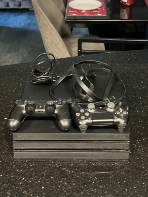 PlayStation 4 Pro - Sony PlayStation 4 Pro med två DualShock 4-kontroller och tillhörande kablar. Konsolen och kontrollerna visar normalt bruksslitage men ser ut att vara i gott skick. Perfekt för gaming med extra prestanda och 4K-stöd och ingår hdmi kabel