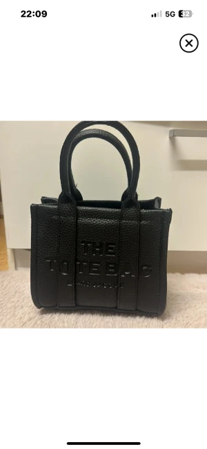 Svart The Tote Bag från Marc Jacobs - Snygg svart handväska från Marc Jacobs, modell The Tote Bag. Väskan är tillverkad i strukturerat skinn med två rejäla handtag och diskret logga framtill. Perfekt storlek för det viktigaste och ger en cool vibe till din outfit.