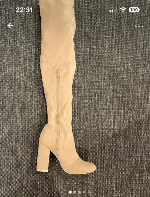Beige overknee stövlar med klack - Säljer ett par snygga beige overknee stövlar med hög klack och rund tå. Stövlarna har dragkedja på insidan och är gjorda i mjuk mocka-look. Perfekta för att lyfta din outfit och ge en trendig vibe.