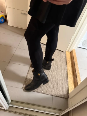 Svarta Tory Burch boots i skinn - Säljer ett par svarta boots från Tory Burch i mjukt skinn med guldfärgad logga på sidan. Perfekta för dig som gillar stilrena detaljer och klassisk design.