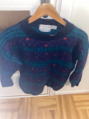 Mörkblå och lila stickad tröja Christopher & Banks - Säljer en stickad tröja från Christopher & Banks i mörkblått och lila med turkosa ränder och små röda prickar. Tröjan är långärmad och har en rund halsringning. Materialet är 50% mohair och 50% akryl, vilket gör den mjuk och fluffig. Perfekt för kyliga dagar!