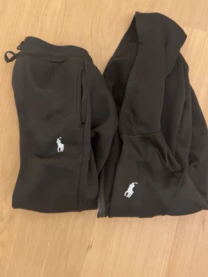 Ralph Lauren svart mjukisset – tröja & byxor – stilrent och bekvämt - Säljer ett snyggt och bekvämt svart mjukisset från Ralph Lauren, bestående av tröja och matchande byxor. Perfekt för både vardag och avslappnade tillfällen. Klassisk design med hög kvalitet och tidlös stil. Storlek S men funkar för M. 	•	Märke: Ralph Lauren 	•	Färg: Svart 	•	Set: Tröja + byxor