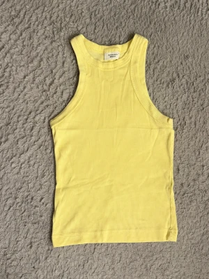Gul topp - Säljer denna söta ljusgula linnetopp från Gina som inte kommer till användning längre. Toppen är ärmlös med rund halsringning och har en slim passform som sitter snyggt mot kroppen. Perfekt för varma dagar och enkel att styla med jeans eller shorts.