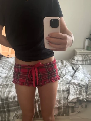 Rödrutiga shorts med volangkant XS - Supersöta rödrutiga shorts från Cubus i storlek XS. De har en låg midja, volangkant nertill och en dekorativ snörning framtill. Mjukt bomullstyg som känns skönt mot huden. Perfekta som mysplagg hemma.