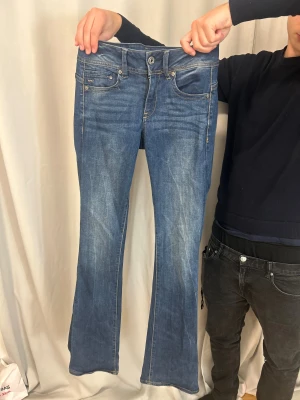 Blå bootcut jeans från G-Star RAW - Snygga blå jeans från G-Star RAW i bootcut-modell med klassisk femficksdesign och ljusa slitningar framtill. Jeansen har normal passform och är tillverkade i jeansmaterial med detaljerade sömmar och logopatch bak i midjan.
