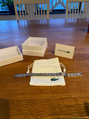 Lacoste armband - En stilrent Lacoste armband i metall Länkar går att ta av om man vill minska storleken.  Ny i nytt skick. Original box tillkommer
