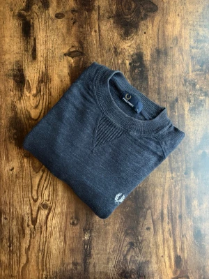 Fred Perry Tröja - Fred Perry tröja i klassisk casuals/old money-stil. Välvårdad och i bra skick utan hål, fläckar eller slitage, den har dock lite missfärgning. Tidlös design med diskret logotyp, stark koppling till brittisk casuals-kultur. Perfekt både till vardag och mer uppklädda outfits. Ett stilrent plagg som aldrig går ur tiden.