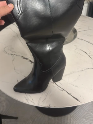 Svarta boots med klack och spetsig tå - Säljer ett par svarta boots i skinn med hög klack och spetsig tå. Snygga sömmar och stäilren design som ger en cool vibe. Perfekta för dig som vill ha ett statement-plagg i garderoben. Passar till många olika outfits och har en stabil plattform.