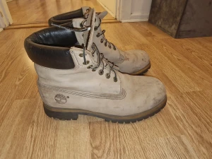 Timberland boots - Säljer ett par klassiska Timberland boots i beige mocka med svart vadderad krage. Skorna har grov platt sula, rund tå och metallöglor för snörning. Timberland-loggan är präglad på sidan. Perfekta för höst och vinter.