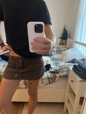 Brun kortkjol med snörning - Säljer en brun kortkjol från Desigual i bomull med coola fickor både fram och bak. Kjolen har snörning i midjan med pärldetaljer och knappstängning. Perfekt för dig som gillar en avslappnad och trendig stil.