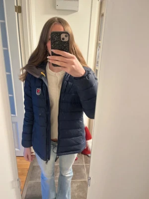 Mörkblå Fjällräven Expedition dunjacka S - Säljer en mörkblå Fjällräven Expedition Series dunjacka i dammodell, storlek S. Jackan har klassisk broderad röd räv-logga på bröstet, gul snörning vid huvan och quiltad design. Perfekt för kalla dagar med sin fluffiga och varma känsla. Jättefint skick! 💗
