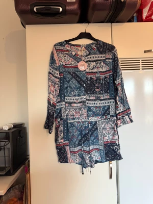 Odd Molly mönstrad byxdress strl 1 - Säljer en snygg byxdress från odd molly. Den har ett unikt blommigt och rutigt mönster i mörkblått, vitt och mörkrött. Byxdressen har långa ärmar, knappar framtill och snörning i midjan. Materialet är 100% viskos. Från märket Odd Molly. Storlek 1 som enligt deras storleksguide motsvarar en S. Helt ny med tags/ prislapp fortfarande kvar.  