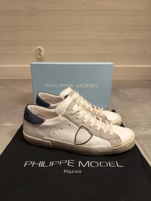 Vita Philippe Model skor - Säljer mina vita Philippe Model skor med blå mocka på hälen. Dem är i nästan helt nytt skick, 8/10. Skorna är i storlek 44 och nypris är ca 3200 kr. Box och dustbag ingår. Skriv för mer bilder eller ifall du har några generella frågor!