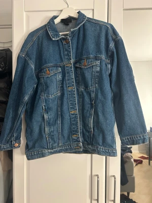 Blå jeansjacka från Monki - Säljer en klassisk blå jeansjacka från Monki i storlek S. Jackan har raka långa ärmar, knappar framtill och två bröstfickor med knapp. Perfekt för dig som gillar en chill och tidlös stil. Passar till allt och är lätt att matcha med andra plagg. Stor i storlek 