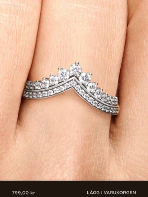 Silvrig tiara ring från Pandora - Säljer en snygg silvrig ring med glittriga stenar från Pandora. Den är inte använd många gånger. Ca 3-4. Den är i välldiht bra skick. Köptes för 900