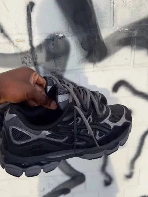 Svarta och grå Asics sneakers - Säljer ett par snygga Asics sneakers i svart och grått med mesh och mockadetaljer. Skorna har rund tå, platt sula och snörning. Perfekta för dig som gillar streetwear och vill ha en stilren look. Box medföljer.